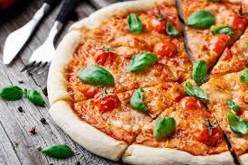 Fresh homemade pizza topped with cherry tomatoes and basil on a wooden table, served with cutlery.
