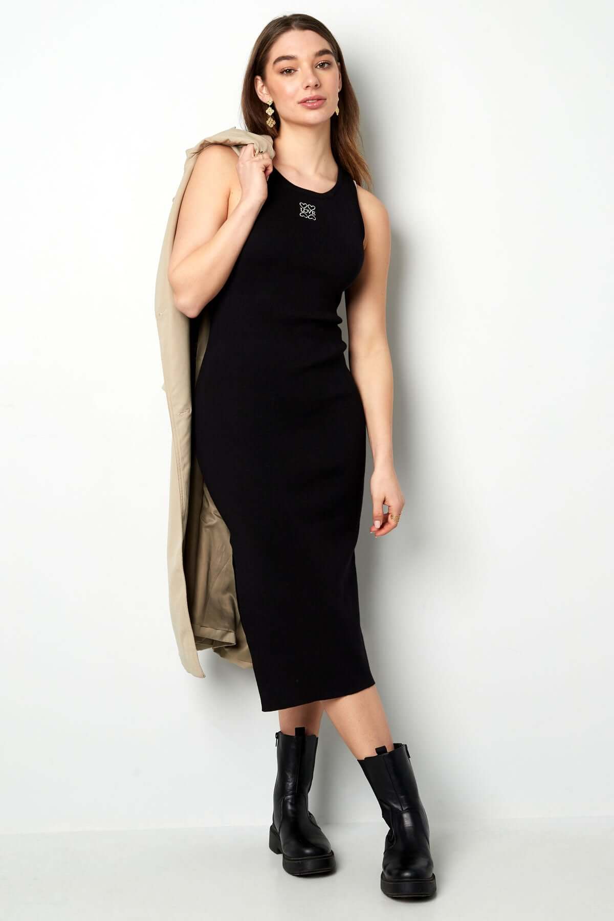 Elegant black bodycon maxi dress with sleeveless design, paired with stylish boots and a statement coat.