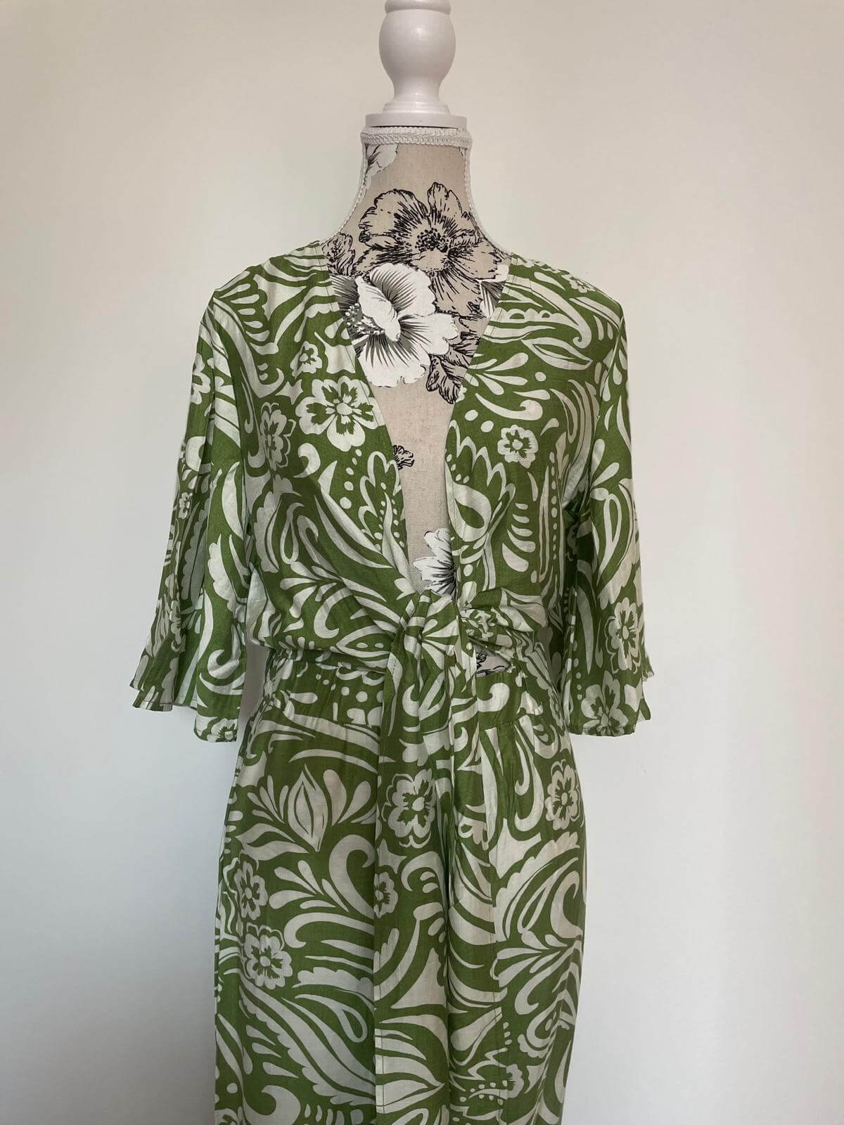 Green and white paisley patterned jumpsuit with short sleeves on a mannequin.